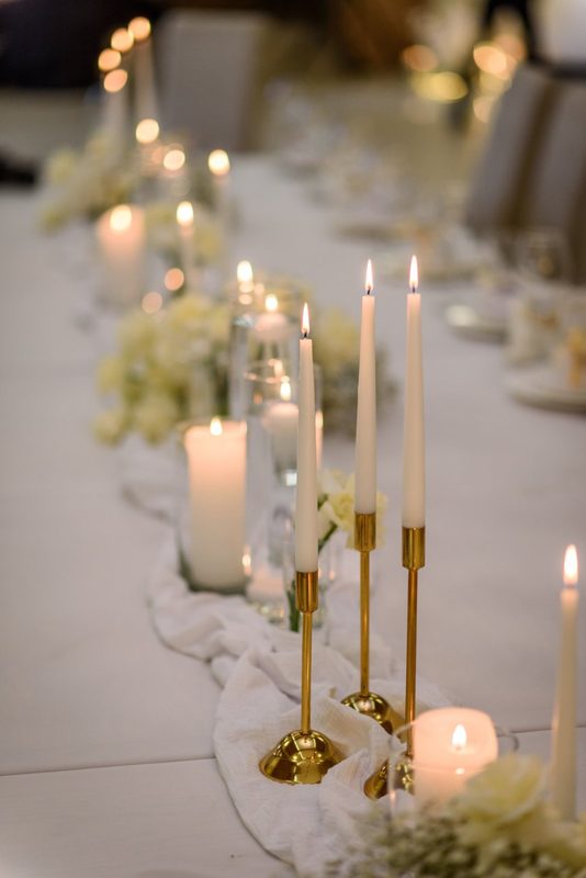Long dinner table lit with taper candles in brass holders